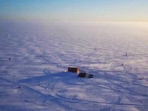 glace-lacstjean-paysage-hiver-activite-village-sur-glace photo de drone de paysage du lac saint jean en hiver sur la glace avec location de cabane à pêche et transport en motoneige pour la pêche blanche au doré et brochet